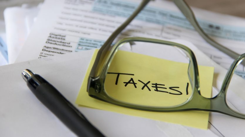 The word Taxes through the glasses of a person filing taxes with tax forms in background